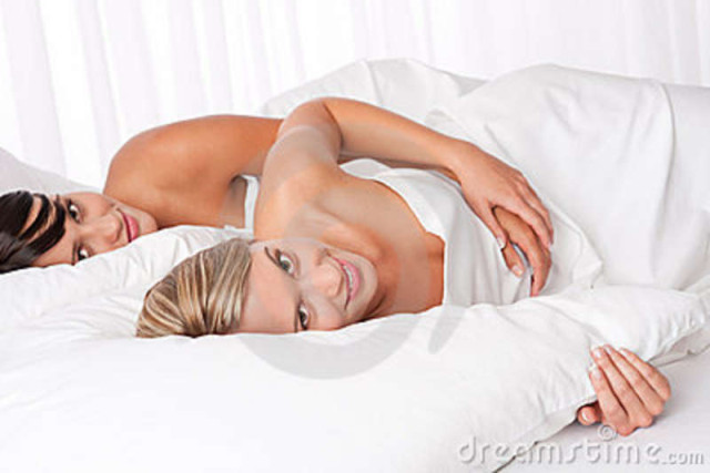 two-young-women-lying-down-white-bed-10757043