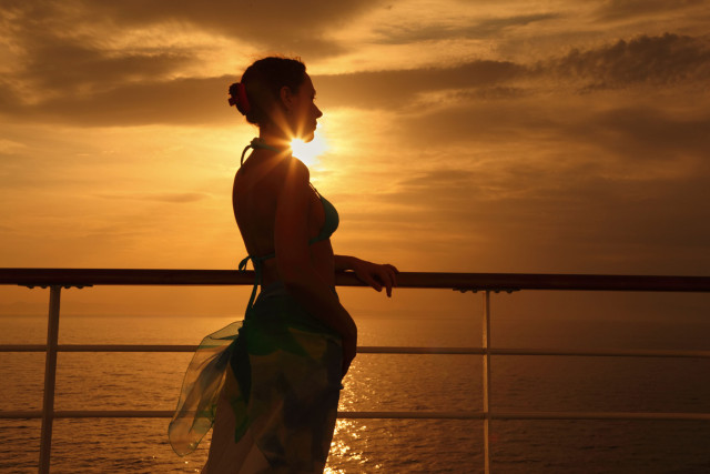 Woman standing on deck of cruise ship and looking away.