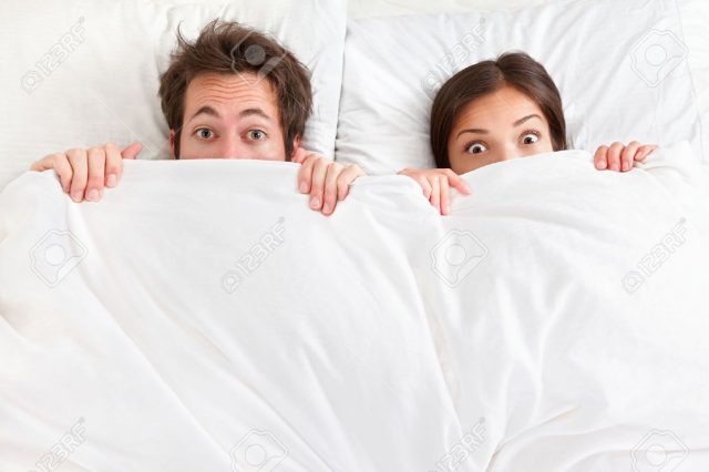 12903060-Funny-couple-in-bed-looking-and-peeking-over-sheets-surprised-Young-interracial-couple-Asian-woman-C-Stock-Photo